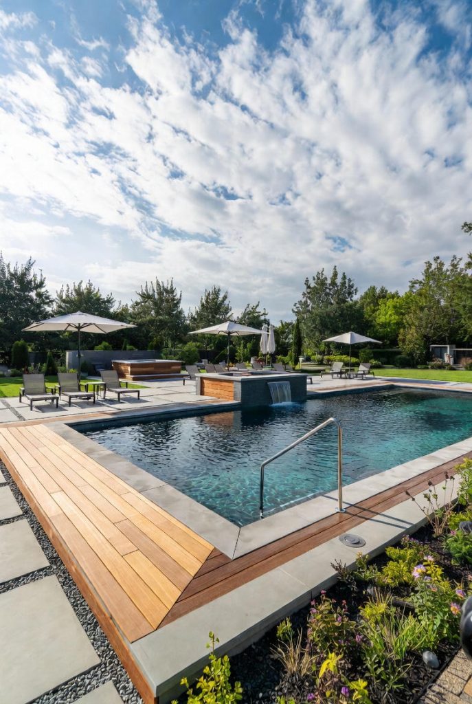 Premium rectangular pool 2026 with durable exotic wood decking, recycled natural stone coping, integrated waterfall, and crystal-clear water thanks to eco-friendly filtration—a symbol of the return to quality materials in France.