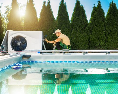 Professional pool technician working on a heat pump installation beside a modern private swimming pool, illustrating the growing technical complexity and specialization in the pool industry in France and Belgium