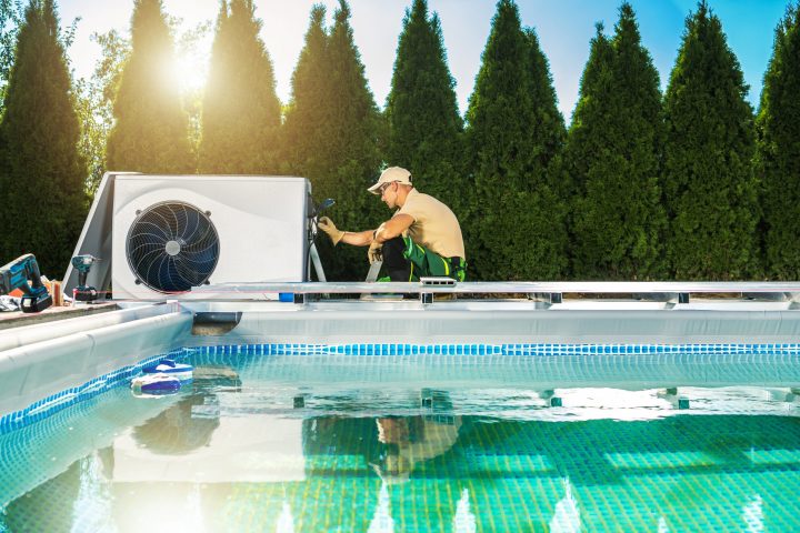 Professional pool technician working on a heat pump installation beside a modern private swimming pool, illustrating the growing technical complexity and specialization in the pool industry in France and Belgium