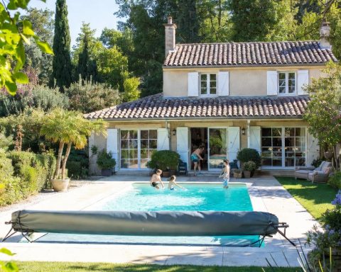 Family pool secured with mandatory safety devices including barrier, safety cover, pool alarm and enclosure, with parents supervising children