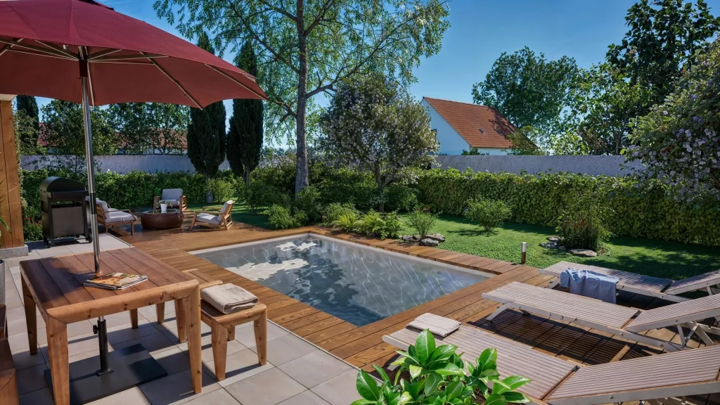 Ibiza rectangular shell pool (Aquaviva 2 compact model) installed with a wooden deck in a small garden.