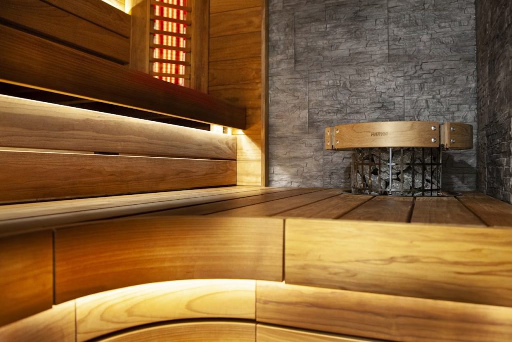 Modern sauna interior featuring a Harvia integrated heater with safety railing and warm LED accent lighting under curved wooden benches.
