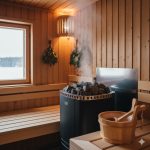 Authentic Finnish sauna interior featuring a traditional heater with volcanic stones, rising löyly steam, and wooden bucket accessories.