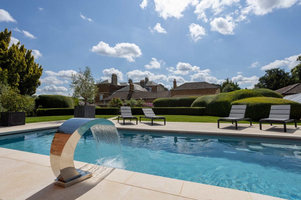 Ein luxuriöser Fiberglas-Schwimmbecken von Aqua Technics Pools mit modernem Wasserfall und eleganter Landschaftsgestaltung.