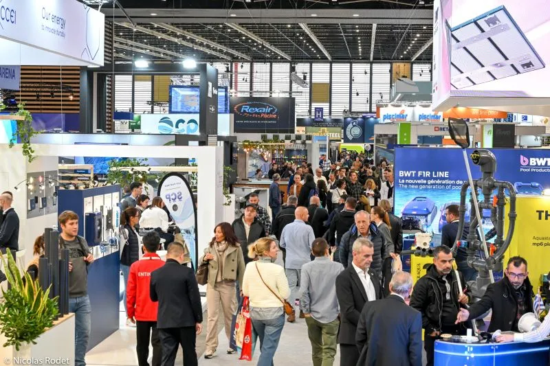 Weitläufige Panoramasicht auf die Hauptausstellungshalle der Piscine Global Messe in Eurexpo Lyon, mit überfüllten Gängen, mehreren modernen Ständen für Pool- und Spa-Aussteller, Fachleute beim Networking und Umhergehen, dynamische Atmosphäre der internationalen Pool-, Spa- und Wellnessbranche.