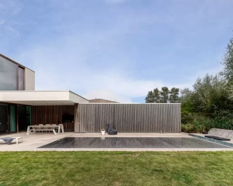 Aquadeck automatische Lamellen-Poolabdeckung vollständig ausgefahren auf einem zeitgenössischen Luxus-unterirdischen Schwimmbecken, nahtlos integriert in moderne Architektur mit klaren Linien, Terrasse und hochwertigem Design, hervorhebend Energieeffizienz, Sicherheit, Langlebigkeit und ästhetische Anziehungskraft für professionelle Poolbauer.