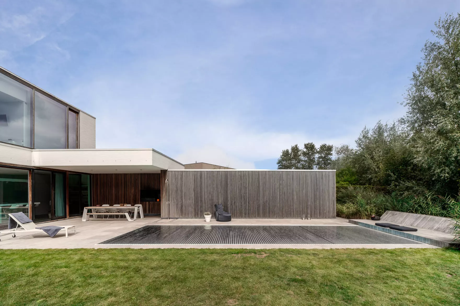 Aquadeck automatische Lamellen-Poolabdeckung vollständig ausgefahren auf einem zeitgenössischen Luxus-unterirdischen Schwimmbecken, nahtlos integriert in moderne Architektur mit klaren Linien, Terrasse und hochwertigem Design, hervorhebend Energieeffizienz, Sicherheit, Langlebigkeit und ästhetische Anziehungskraft für professionelle Poolbauer.