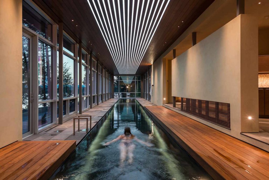 High-end indoor swimming pool featuring extensive warm wood architecture, high beamed ceiling and natural light, perfect example of sustainable wood-powered pool heating