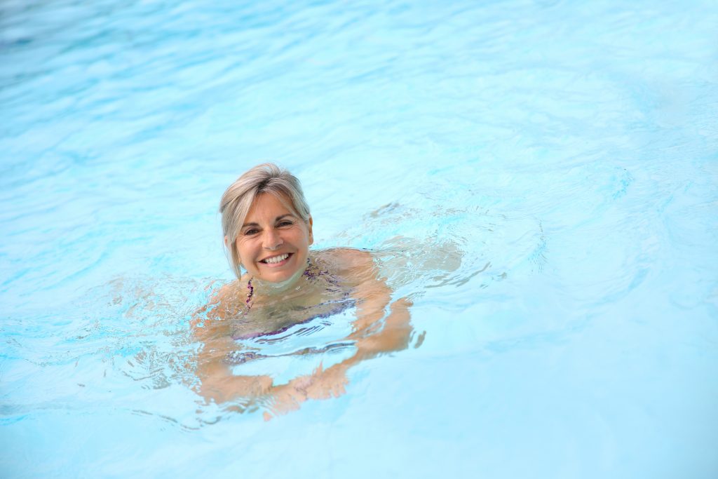 A smiling woman swimming in bright blue water, looking directly at the camera.