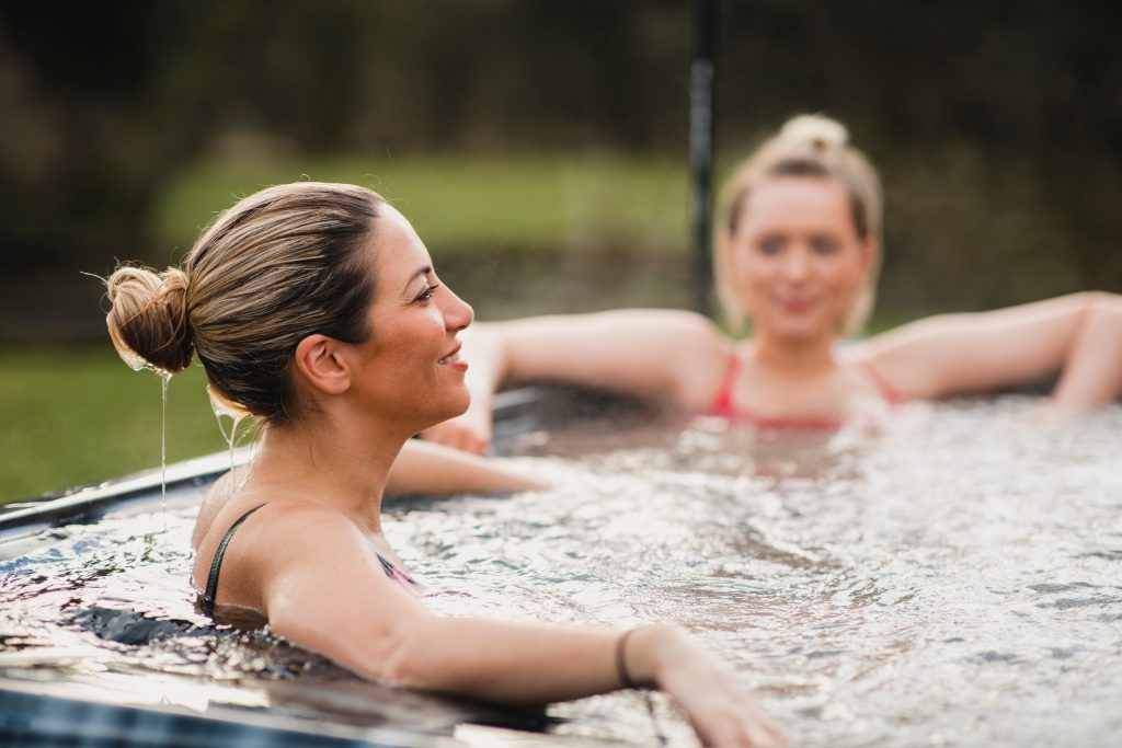 Two women smiling and relaxing in a modern hot tub outdoors.