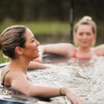 Two women smiling and relaxing in a modern hot tub outdoors.