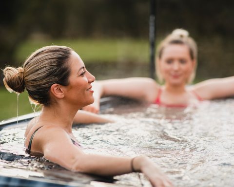 Two women smiling and relaxing in a modern hot tub outdoors.