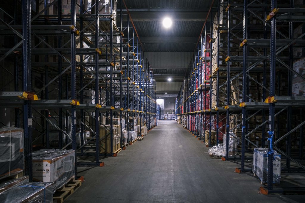 Longue allée centrale de l'entrepôt logistique de Poolstar, avec de hautes étagères chargées de palettes de produits