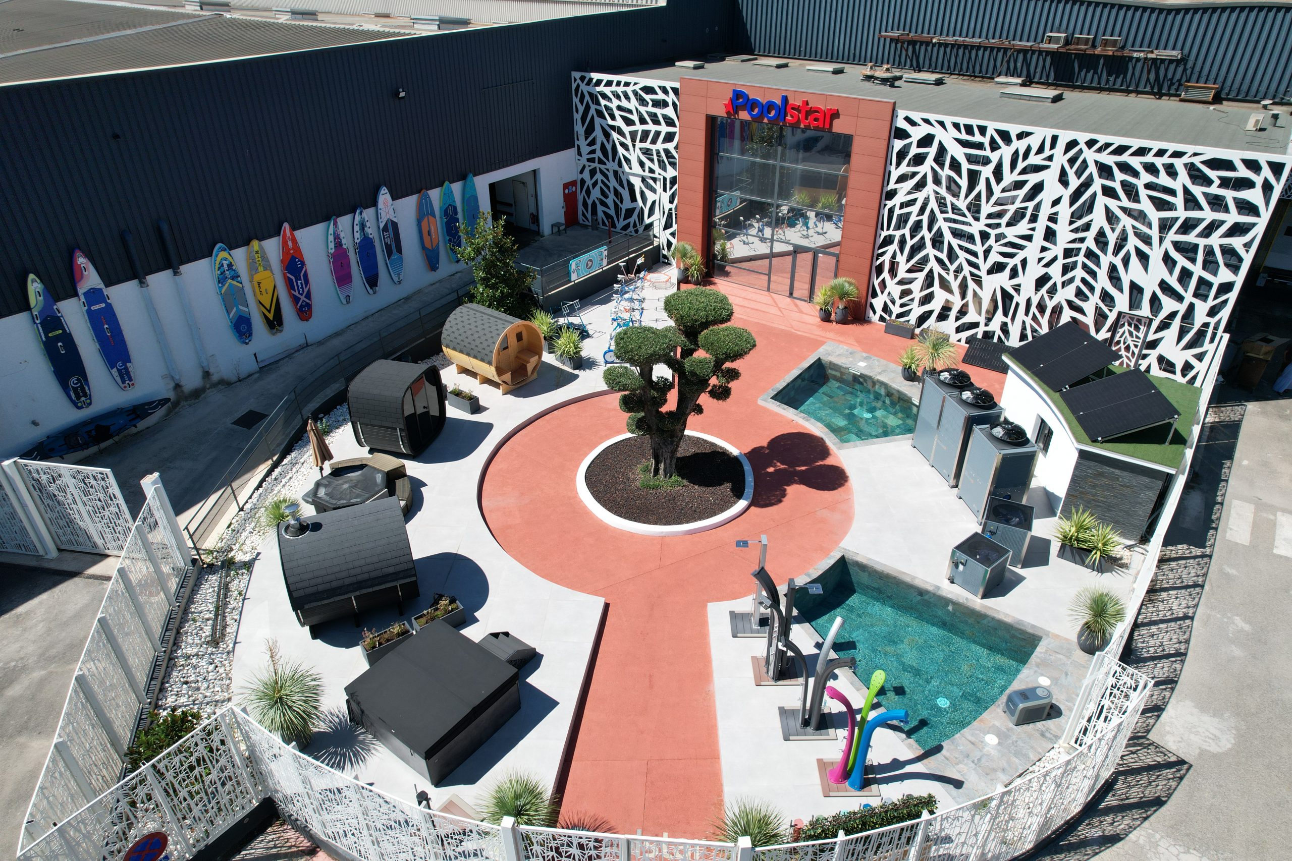Vue aérienne du showroom extérieur de Poolstar avec piscine, saunas et paddles colorés.
