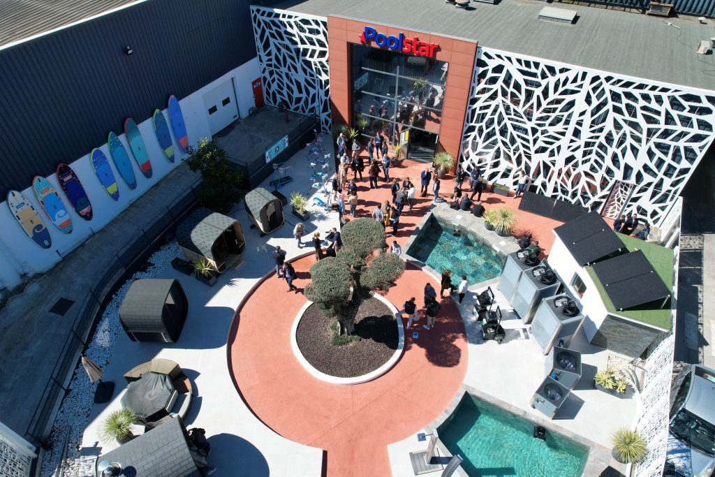 Vue au sol du showroom extérieur Poolstar avec un grand arbre en contre-jour et le logo de l'entreprise en arrière-plan