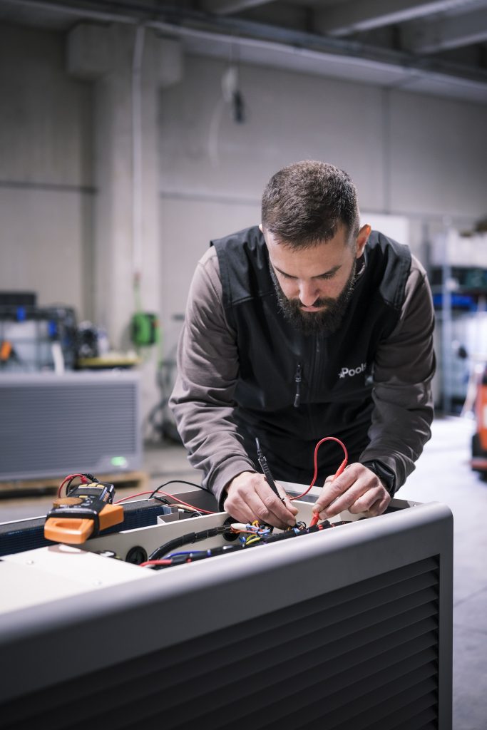 Technicien Poolstar effectuant des tests électriques sur une pompe à chaleur dans l'atelier de Rousset.