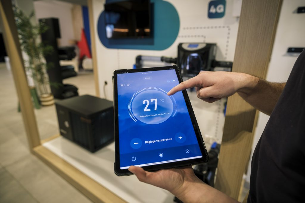 Mains tenant une tablette affichant l'interface de contrôle de la pompe à chaleur Poolex réglée à 27°C
