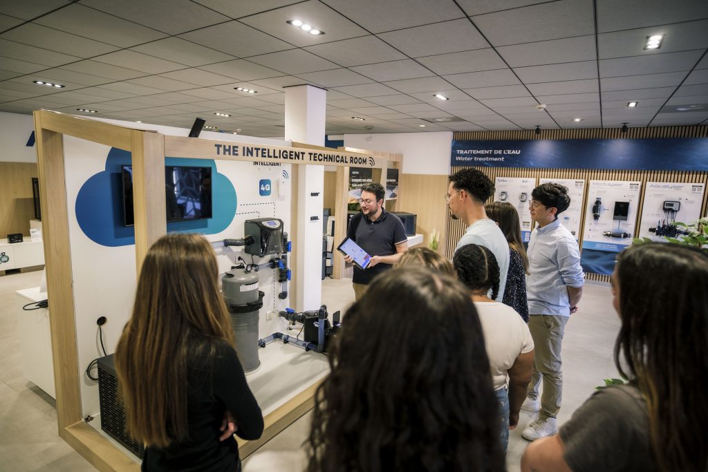Un conseiller Poolstar présente la salle technique intelligente Poolex Nexus à un groupe de visiteurs dans le showroom intérieur