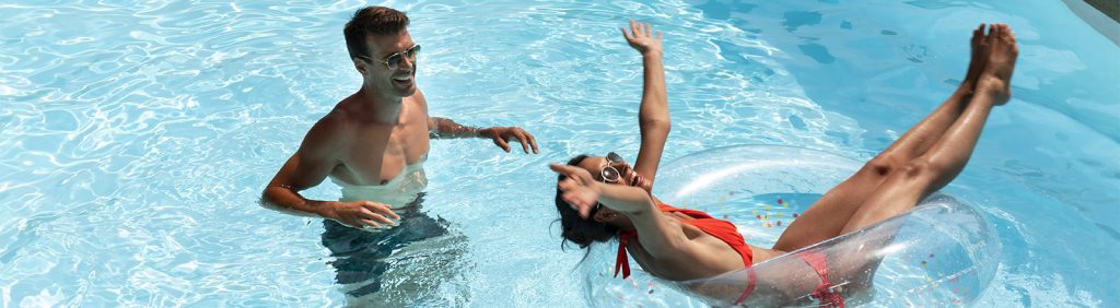 Happy couple enjoying a sunny day in a clear blue swimming pool with inflatable ring