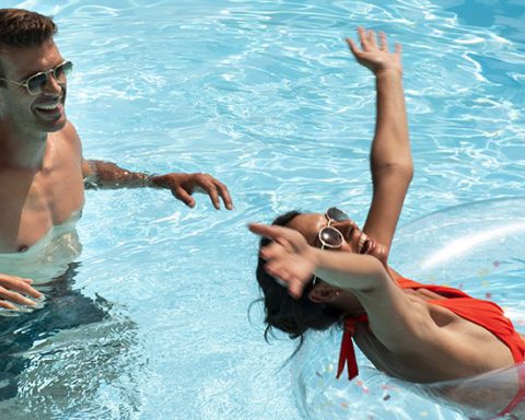 Happy couple enjoying a sunny day in a clear blue swimming pool with inflatable ring