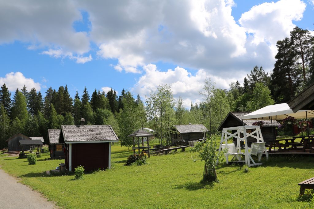 Traditional Finnish smoke sauna village with wooden cabins under a cloudy blue sky.