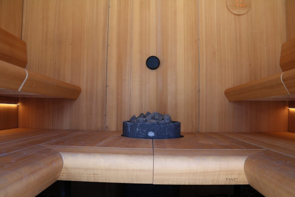 Modern luxury sauna interior with wooden benches and a central stone heater.