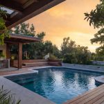 Luxurious modern swimming pool with wooden deck, outdoor kitchen and professional landscaping in a harmonious backyard design.