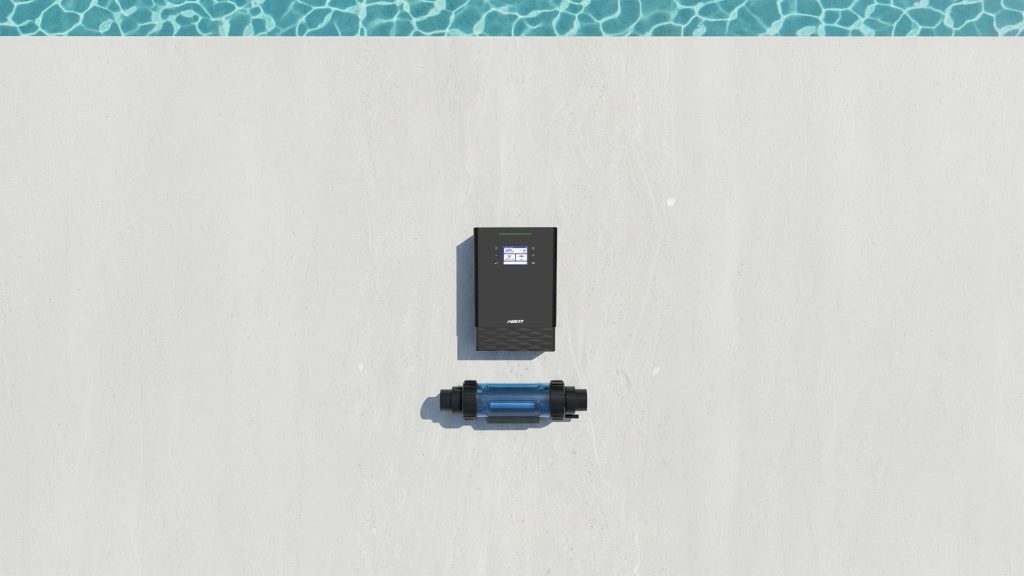 Top-down view of the black Modulyser control panel and its separate transparent blue electrolysis cell lying on a light concrete floor next to pool water.