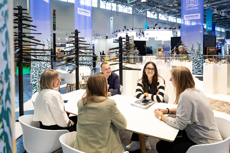 Group (from Sauna From Finland team) of pool and spa industry professionals networking at a meeting table inside Aquanale trade show Koelnmesse Cologne