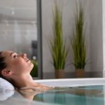 Woman relaxing with eyes closed in a luxury indoor cold water plunge pool with white towel headrest