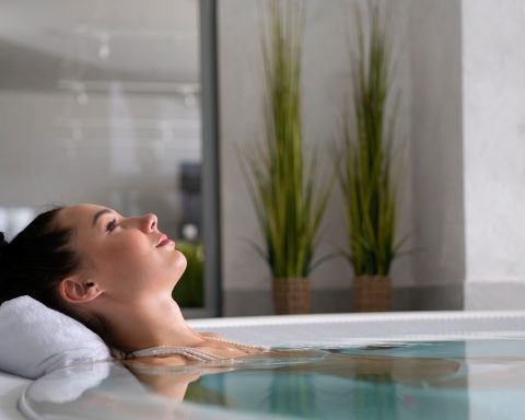 Woman relaxing with eyes closed in a luxury indoor cold water plunge pool with white towel headrest