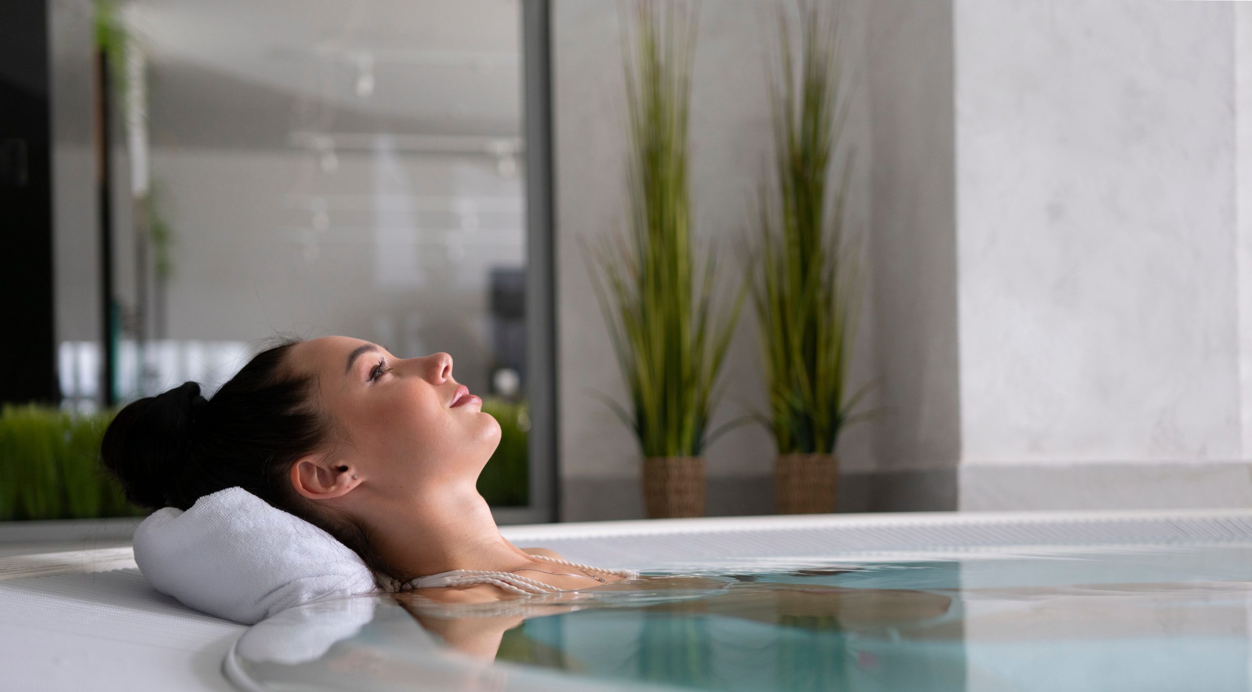 Woman relaxing with eyes closed in a luxury indoor cold water plunge pool with white towel headrest