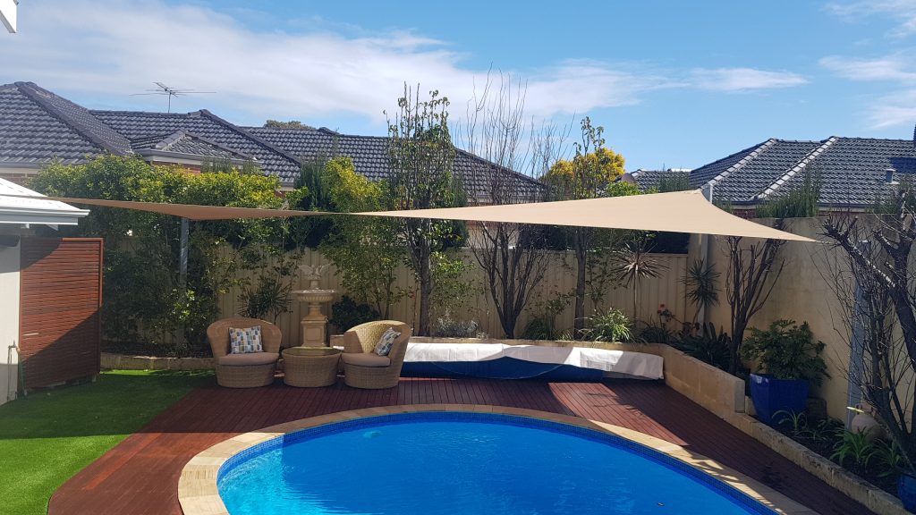 Beige shade sail canopy stretched over a backyard swimming pool and patio area.