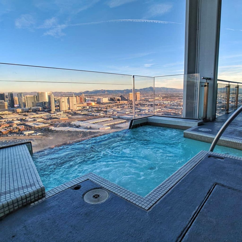 An urban hotel rooftop infinity pool overlooking a sprawling city skyline at sunset.