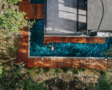 Aerial drone shot of a lap pool surrounded by modern wooden decking and lush green tropical foliage.