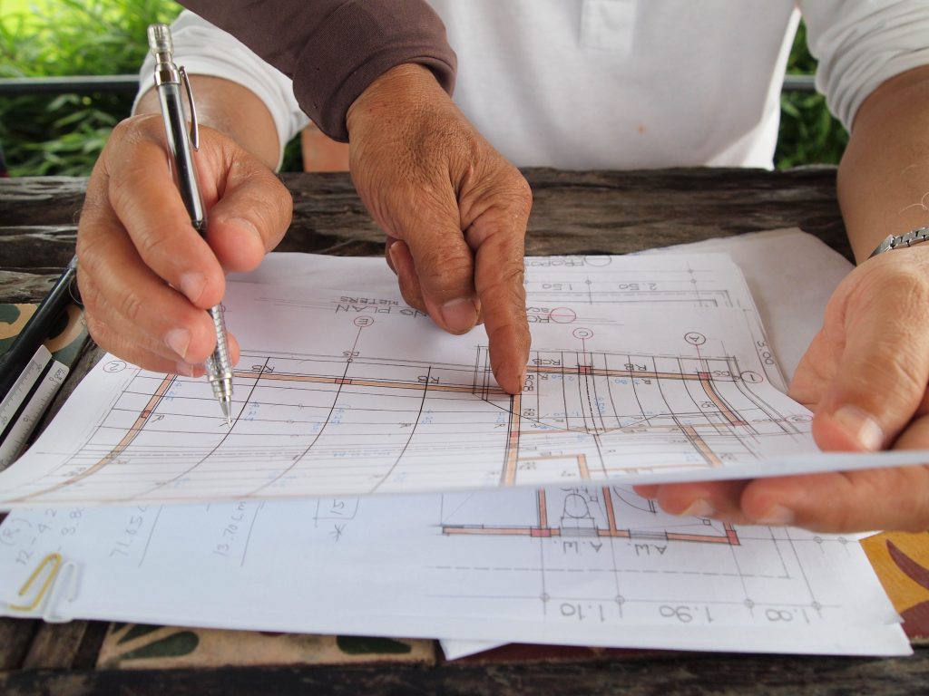 Close-up of two pairs of hands reviewing a technical architectural plan for a swimming pool with a pen.