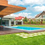 A modern rectangular swimming pool integrated into a contemporary house design with wooden cladding and a deck.