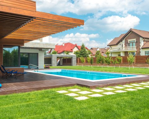 A modern rectangular swimming pool integrated into a contemporary house design with wooden cladding and a deck.