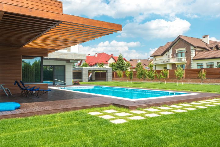 A modern rectangular swimming pool integrated into a contemporary house design with wooden cladding and a deck.