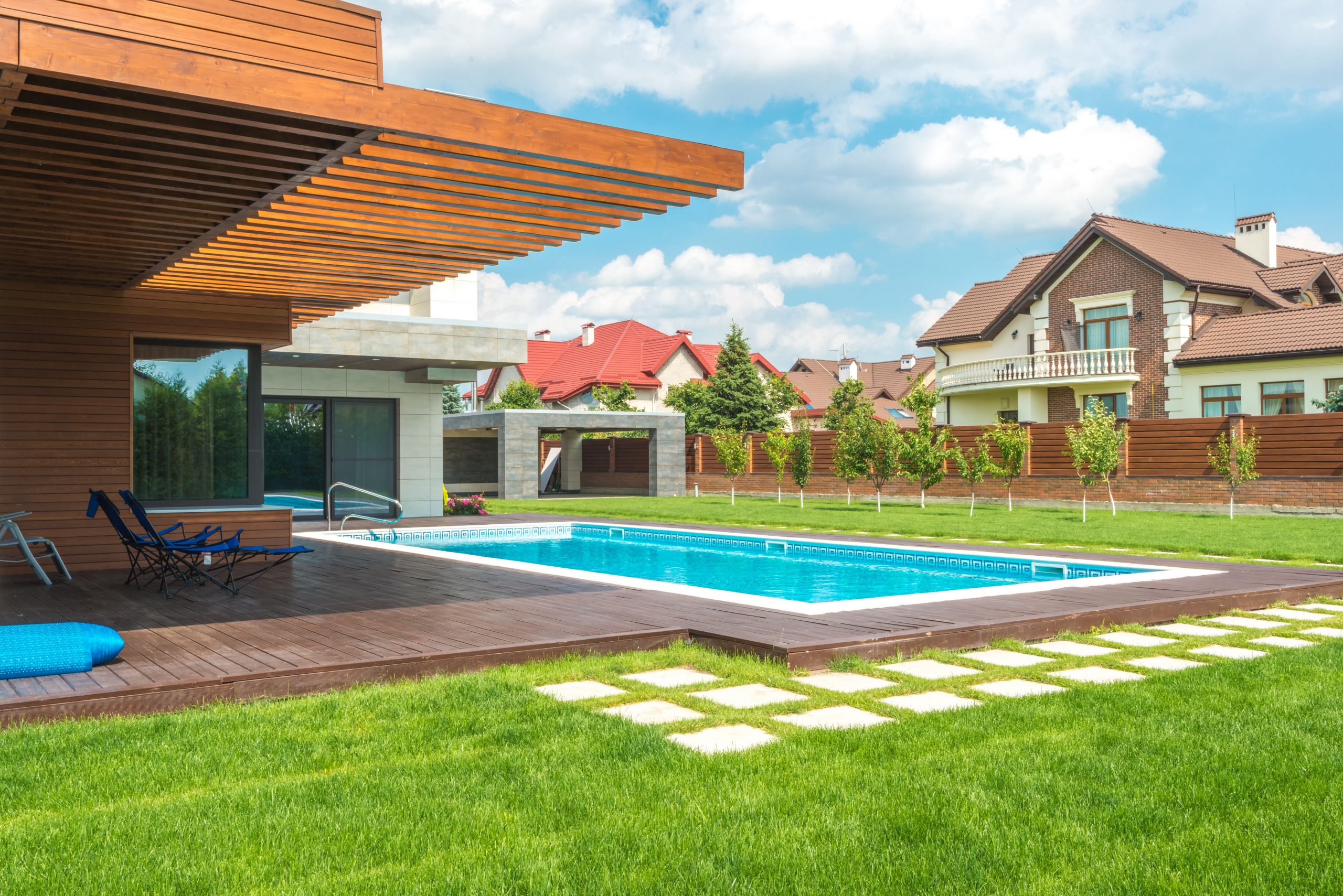A modern rectangular swimming pool integrated into a contemporary house design with wooden cladding and a deck.