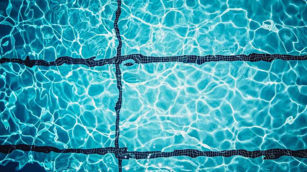 Top-down view of sunlit, shimmering crystal-clear blue water in a commercial swimming pool.