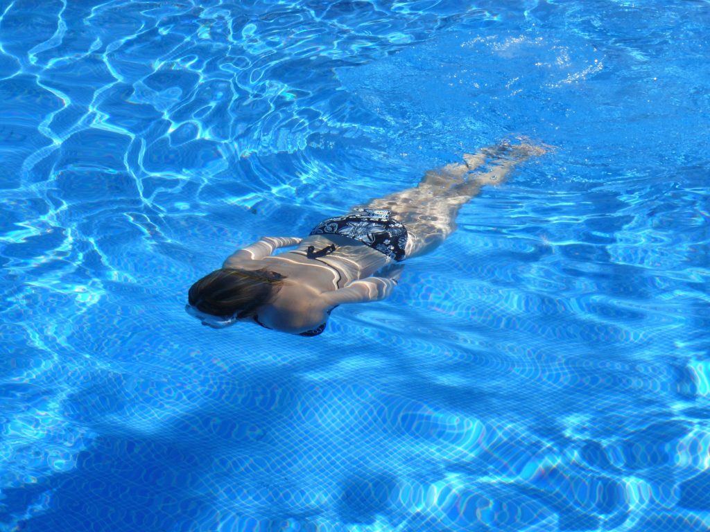 A woman wearing a swimsuit swimming underwater in a crystal clear blue swimming pool during summer