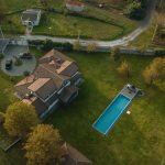 Drone shot of a large residential property with a long rectangular swimming pool in a green lawn.