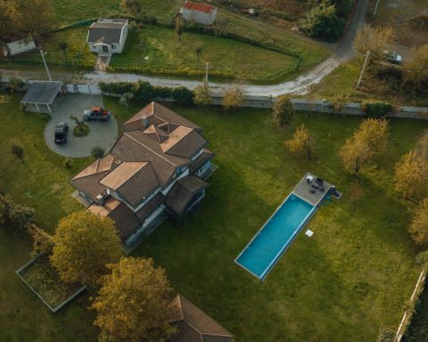Drone shot of a large residential property with a long rectangular swimming pool in a green lawn.