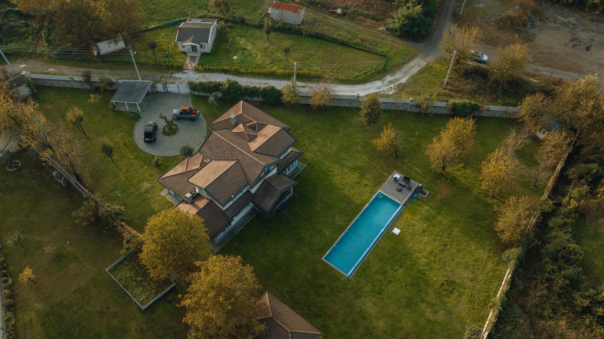 Drone shot of a large residential property with a long rectangular swimming pool in a green lawn.