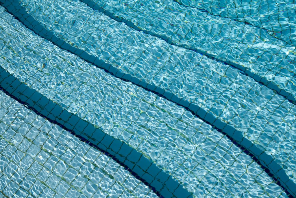 Tiled swimming pool steps viewed through clear, sunlit rippling water