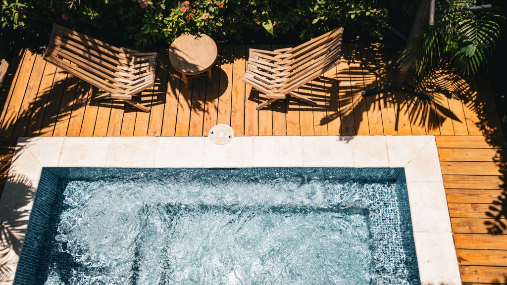 Top-down view of a small rectangular plunge pool with bubbling water next to a wooden deck and lounge chairs.