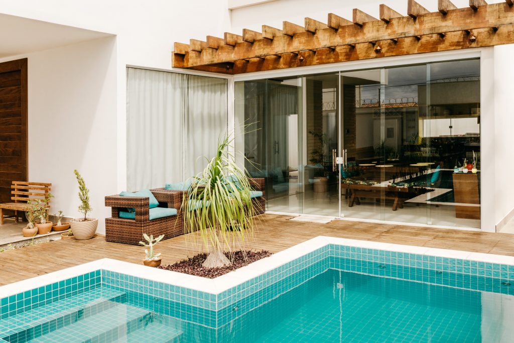 Modern residential swimming pool with turquoise tiles and a wooden deck outside a contemporary house