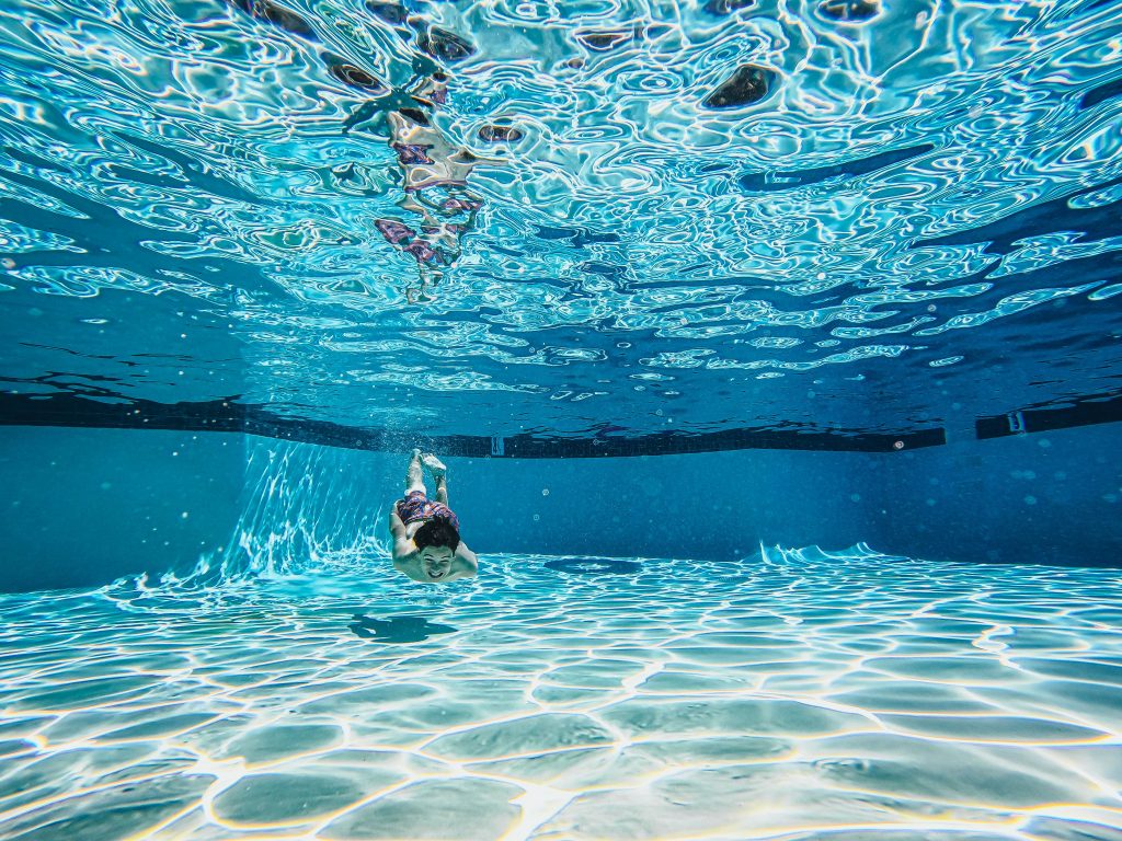 Young boy swimming underwater in a crystal clear residential swimming pool during summer
