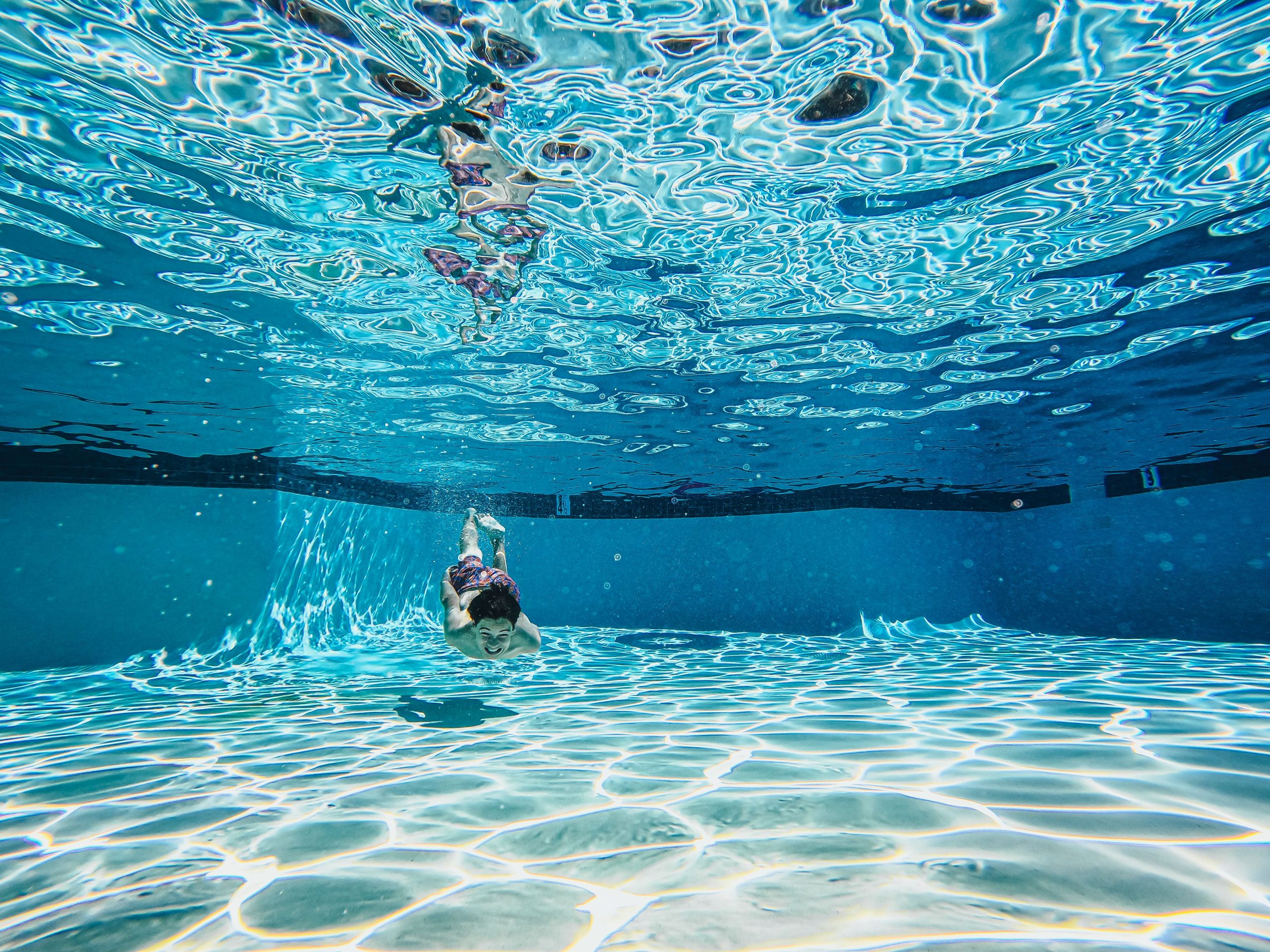 Young boy swimming underwater in a crystal clear residential swimming pool during summer
